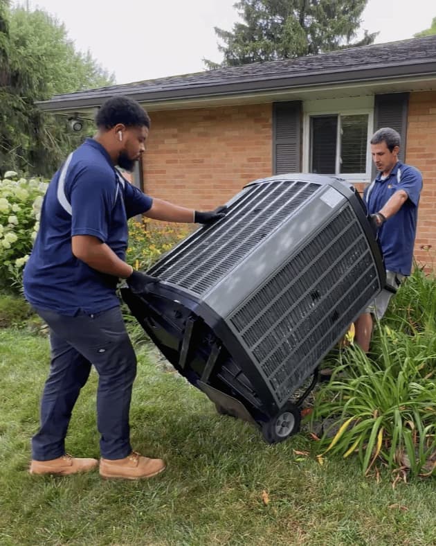 Two people moving an outdoor condenser on a hand truck