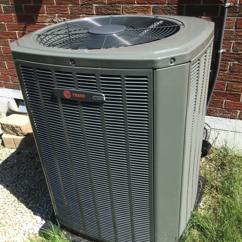 Outdoor Trane central air conditioner condenser beside a brick home